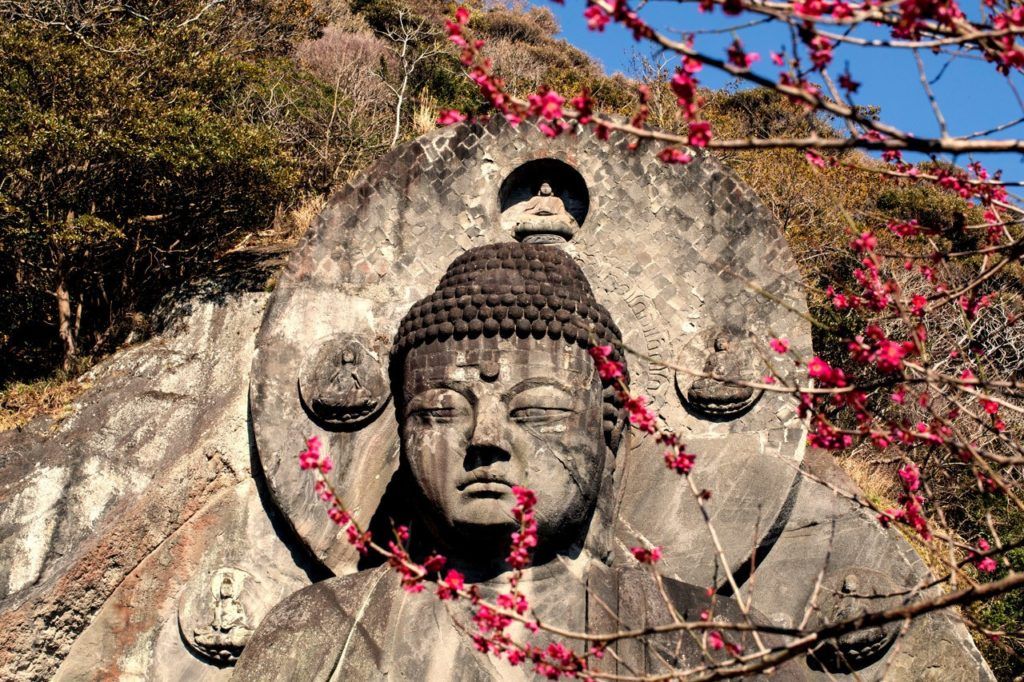 Large Buddha carving with tree blossoms high atop Mount Nokogiri.