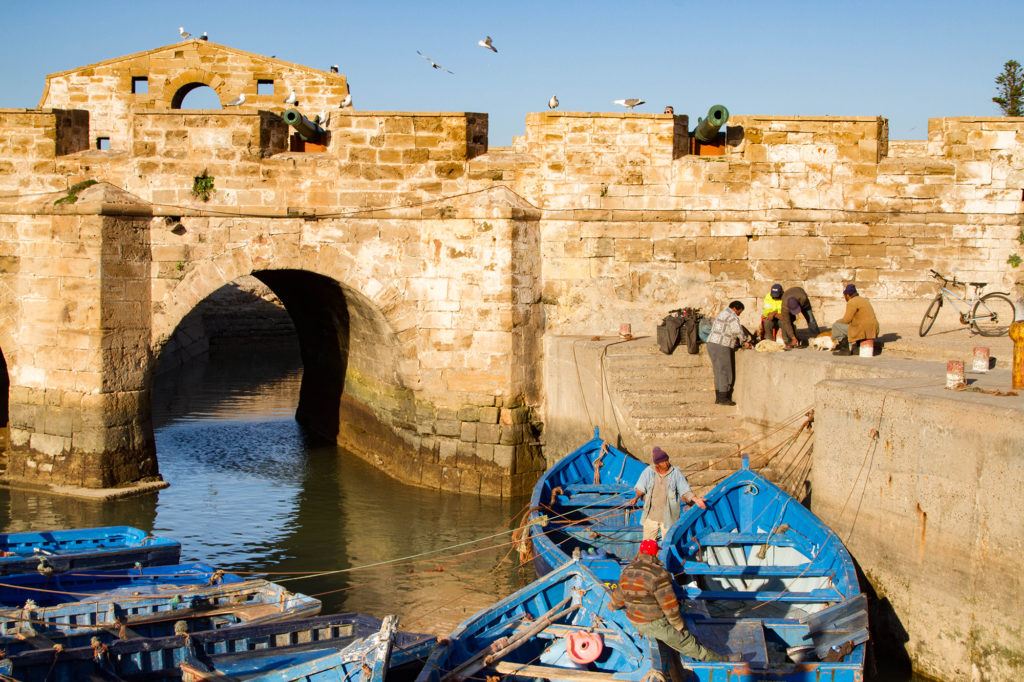 A group of fisherman on the fortress wall preparing their gear and loading their blue boats.
