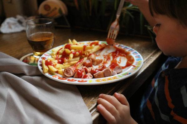 Little boy eating wurst and fries.
