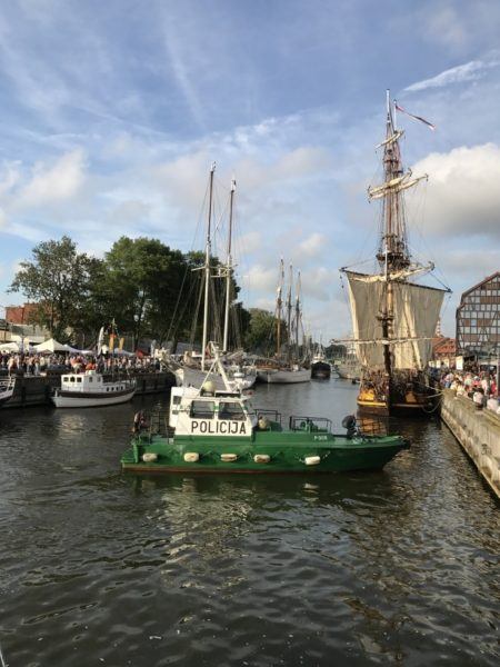 A police boat in harbor with tall ships.
