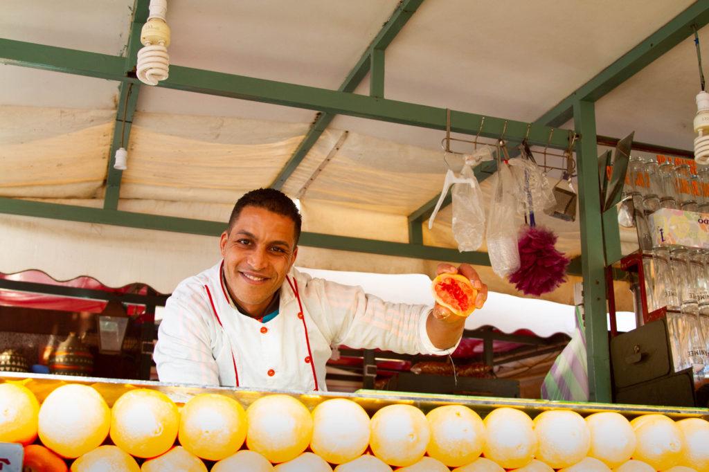 A Jemaa el Fna food stall vendor holds up half a grapefruit to show the freshness of his fresh-squeezed juice.