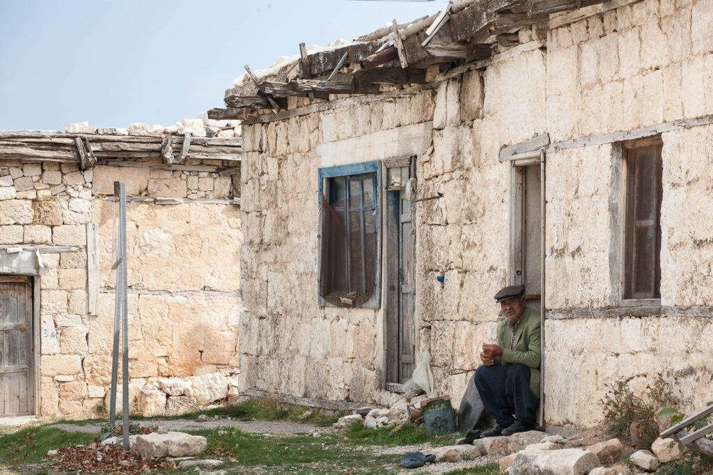 This old man is sitting near the Uzuncaburç parking lot waving people in.