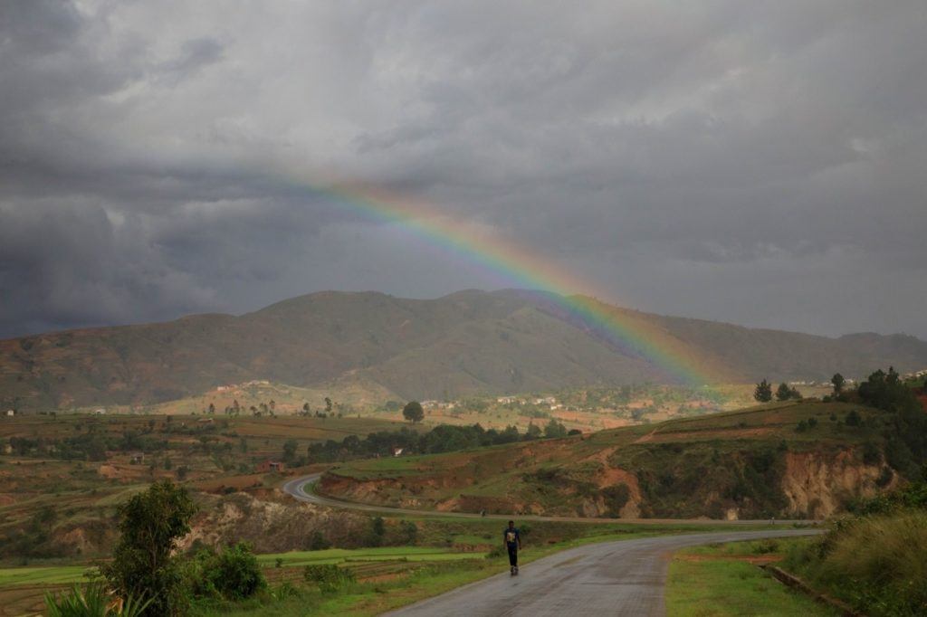 A man walks down a road in Madagascar under a rainbow.