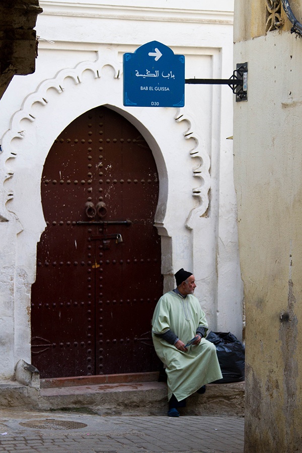 A man in traditional clothing waits at an intricately carved door.