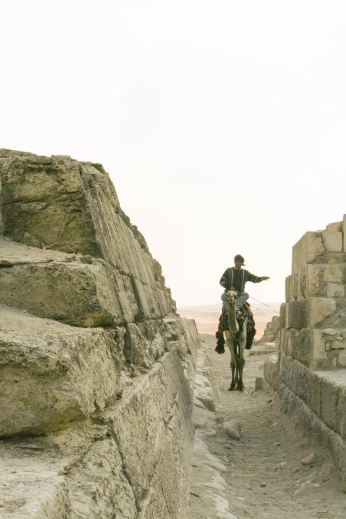 Man riding camel through pyramids alley.