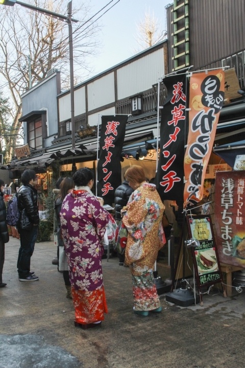 Two women walk down the street trying foods.