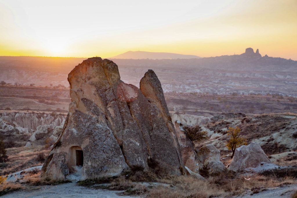 The setting sun silhouettes Uchisar Castle on a distant hill in Uchisar, Turkey.