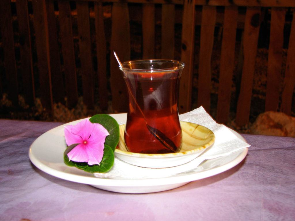 A glass of Turkish tea is elegantly served on a saucer with a pink flower.