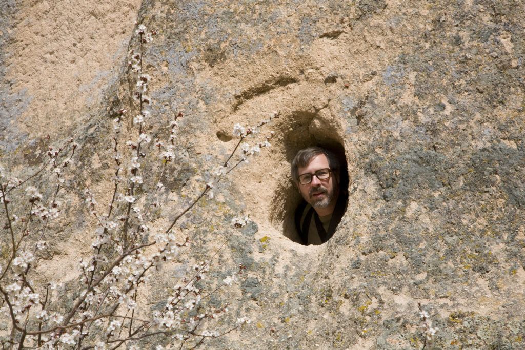 Jim peering out of a small opening in a rock cave.