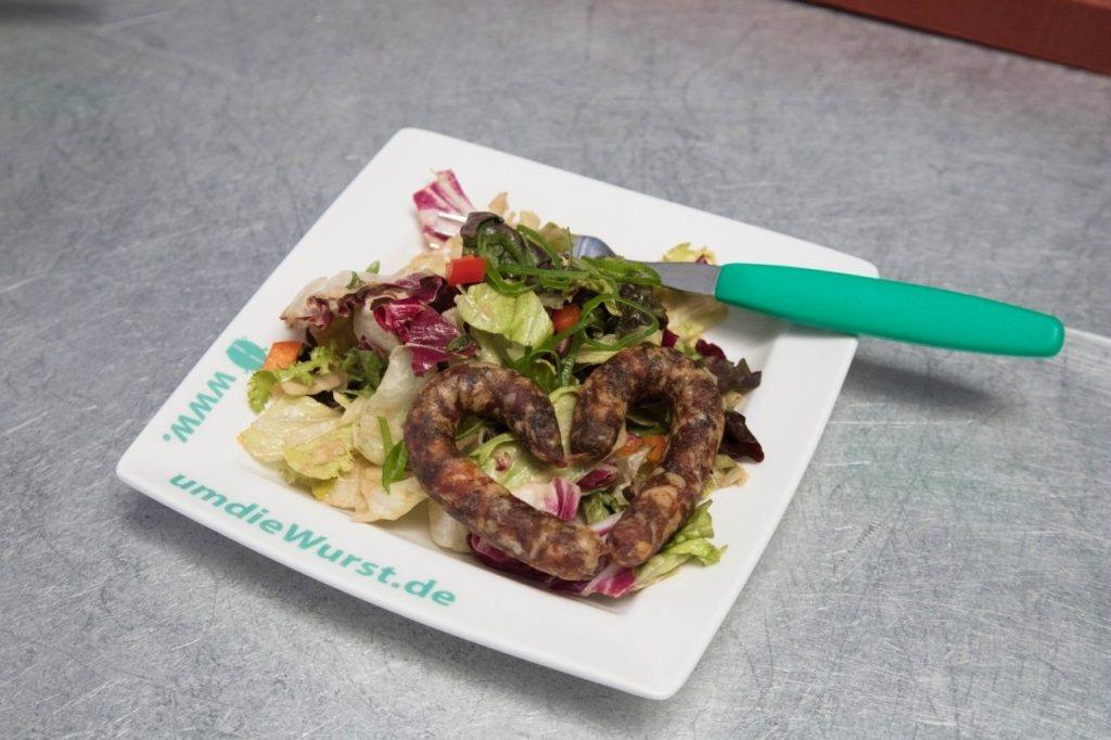  A heart-shaped bratwurst and salad on a plate.