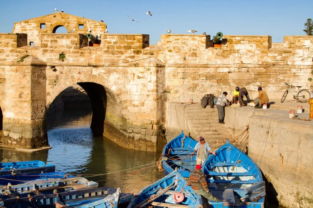 A group of fisherman on the fortress wall preparing their gear and loading their blue boats.