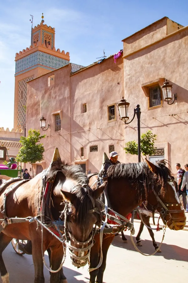 A pair of horses pulling a cart past the Koutoubia Mosque in Marrakesh, Morocco.