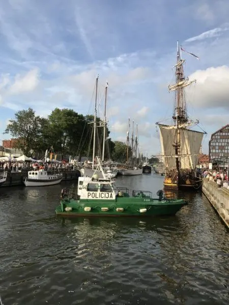 A police boat in harbor with tall ships.