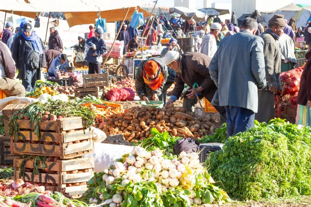 Big crates and huge piles of vegetables with lots of buyers and sellers at the Berber market.