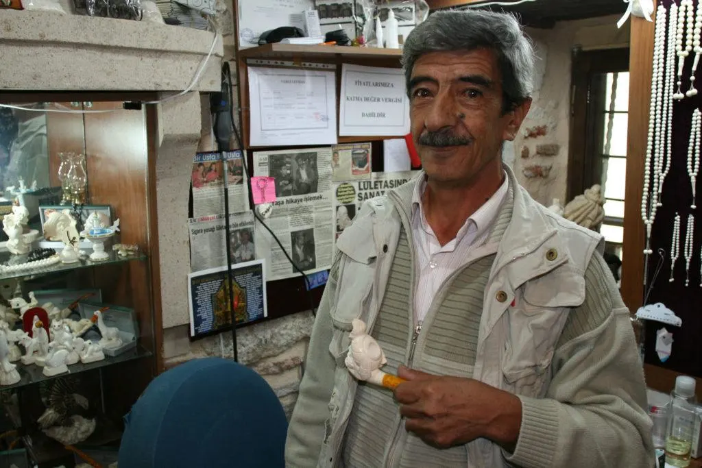 An artist holding a pipe intricately carved from a chunk of Meerschaum, a white, chalky, claylike material.