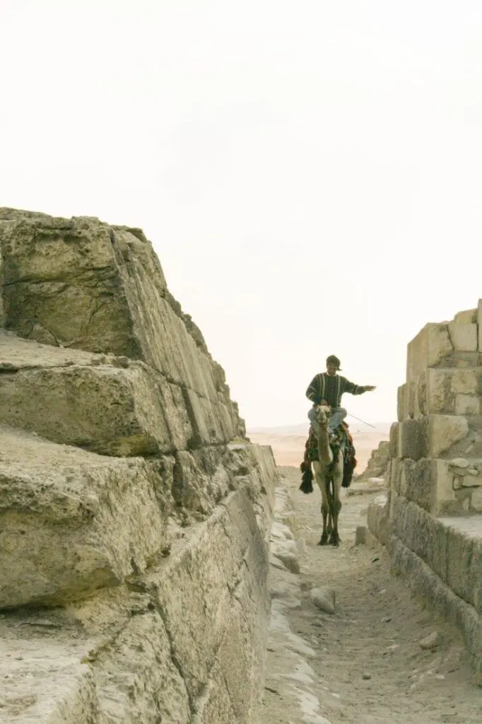 Man riding camel through pyramids alley.
