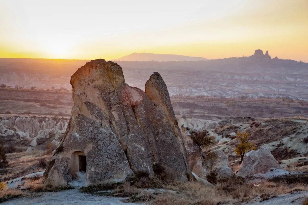 The setting sun silhouettes Uchisar Castle on a distant hill in Uchisar, Turkey.