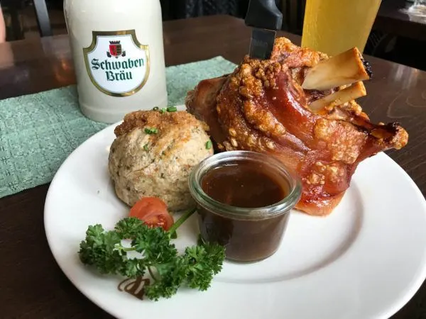 A meal of semmelknoedel, haxen, and sauce with a beer.